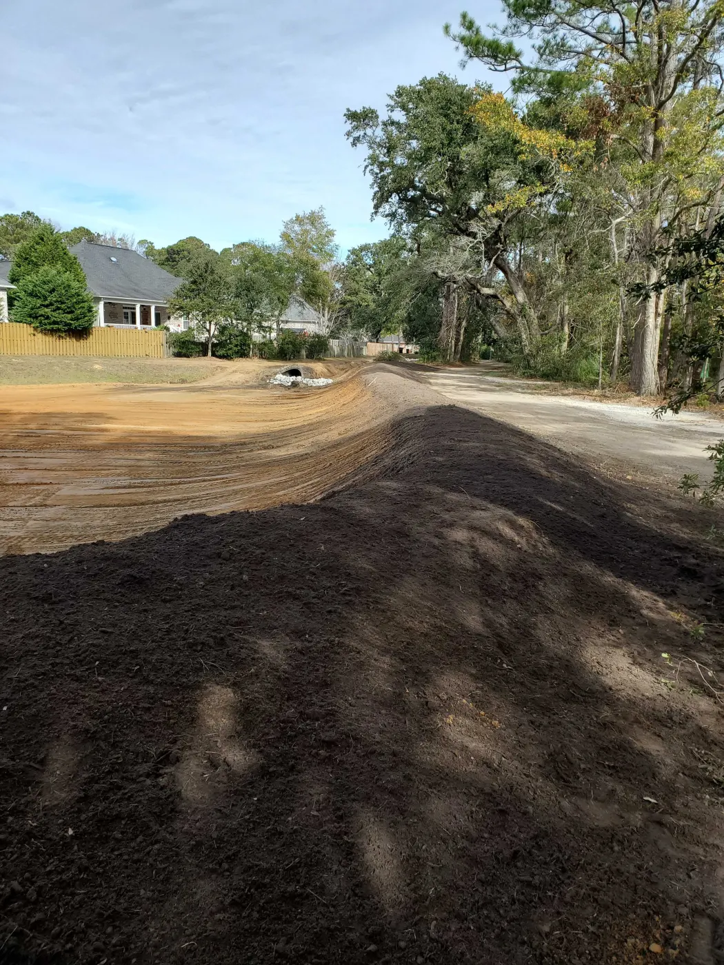 Freshly graded driveway path in dark topsoil between homes, ready for gravel driveway installation near Burgaw, NC
